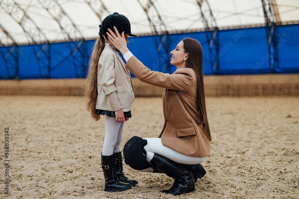 Woman equiping young girl with helmet. Horse lifestyle young kid with helmet.