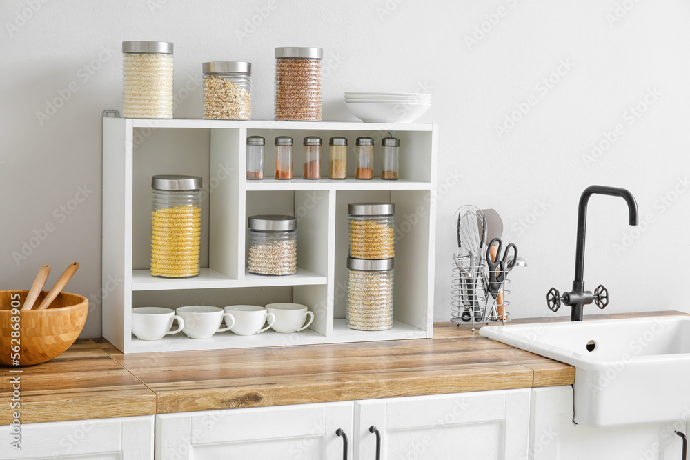 Jars with cereals, spices and utensils on kitchen counter