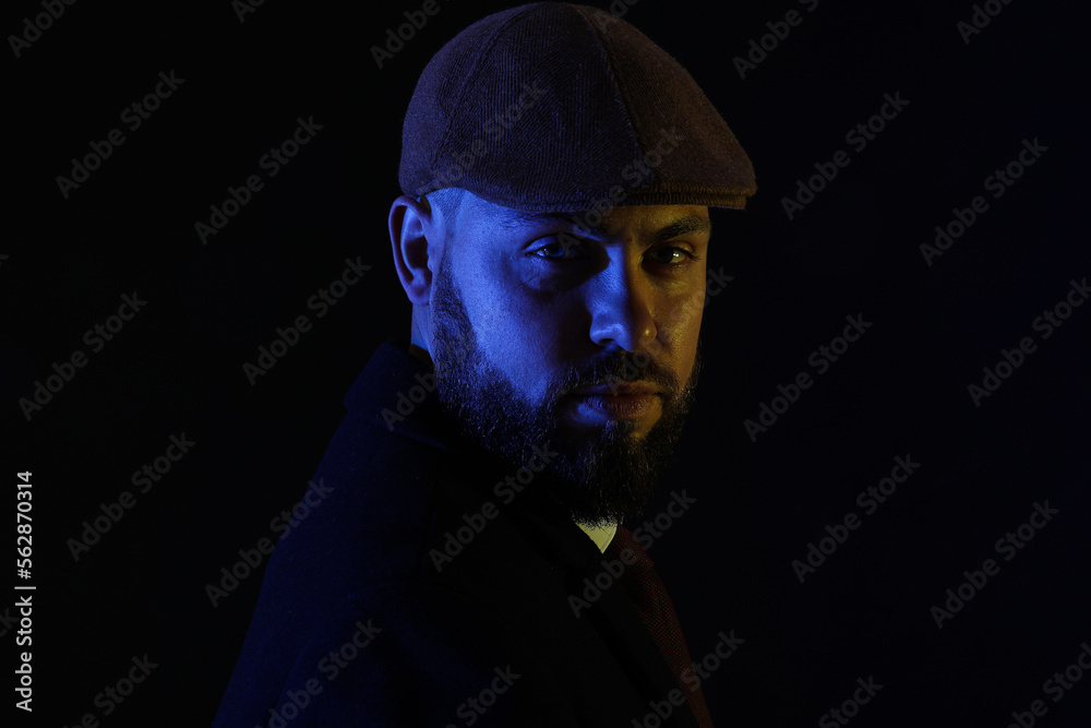 Silhouette of young bearded man in cap on dark background, closeup