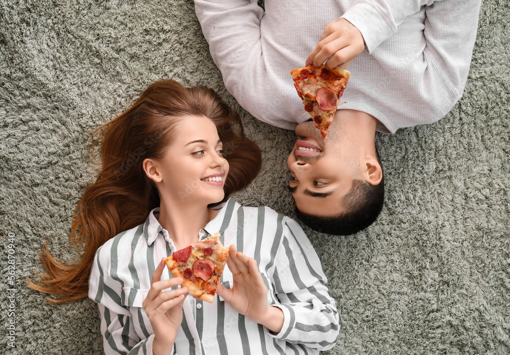 Happy young couple with slices of tasty pizza lying on carpet, top view