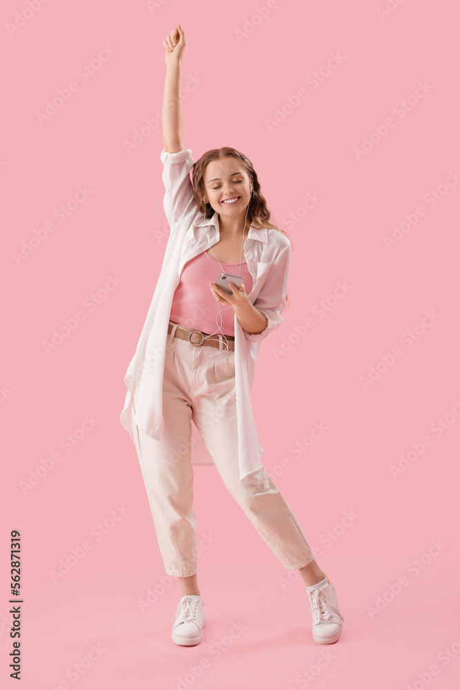 Young woman in earphones with mobile phone listening to music on pink background