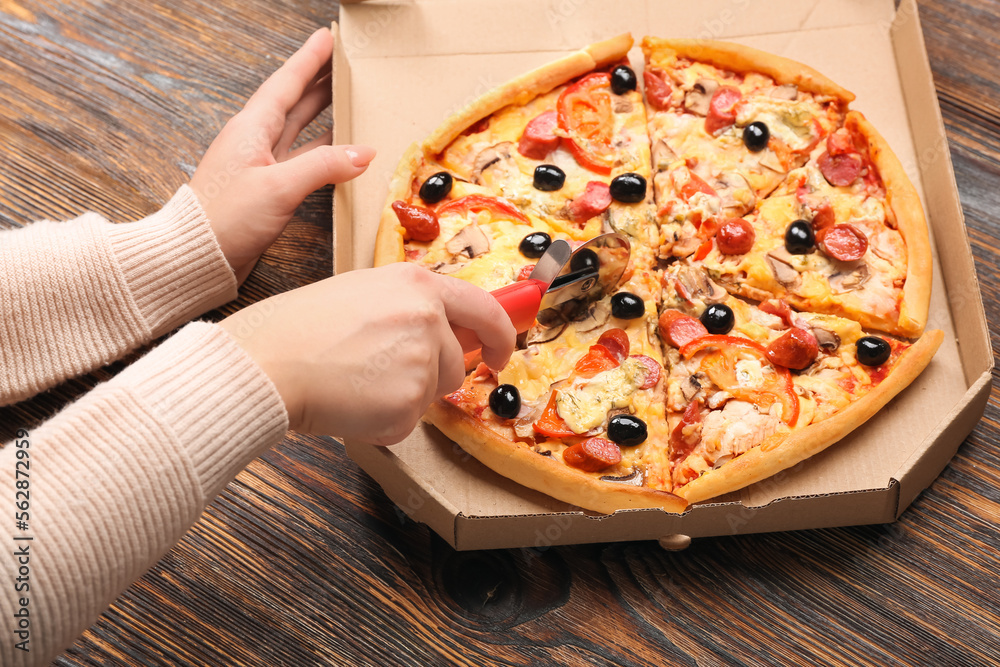 Woman cutting tasty pizza on wooden background, closeup