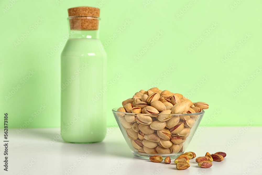 Bowl with nuts and glass of pistachio milk on green background