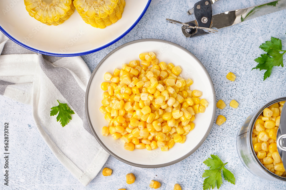 Plates with delicious corn, parsley leaves, tin can and opener on grey table