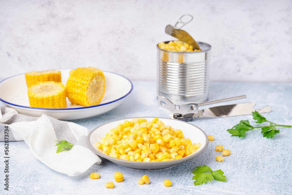 Plates with delicious corn, tin can, parsley leaves and opener on grey table