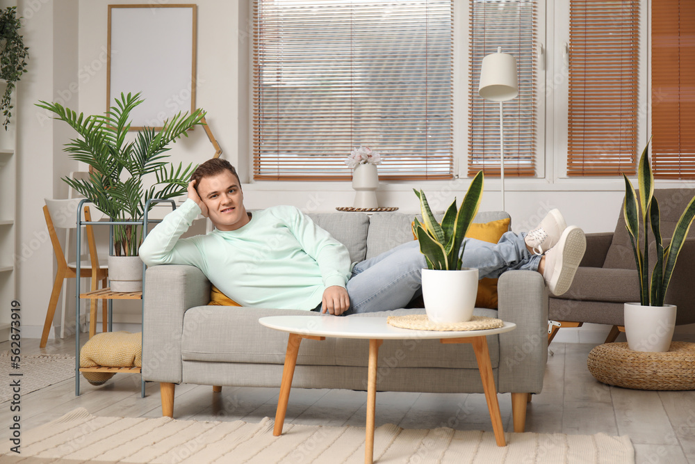 Young man resting on grey couch in living room