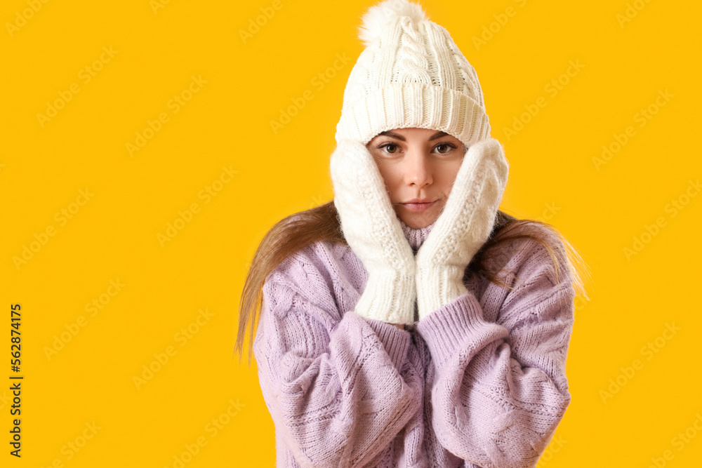 Frozen young woman in winter clothes on yellow background, closeup