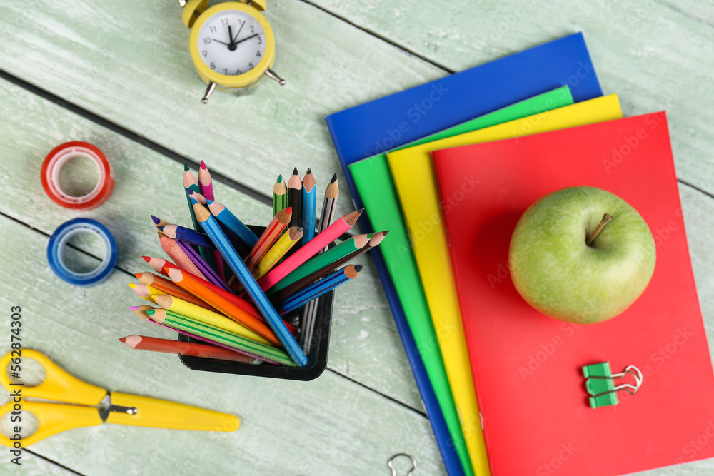 Green apple with notebooks, pencils holder, school stationery and clock on wooden background