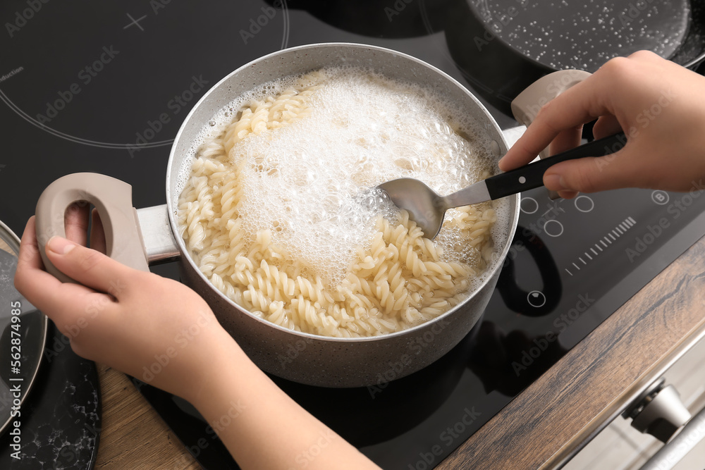 Woman cooking tasty pasta on stove in kitchen, closeup