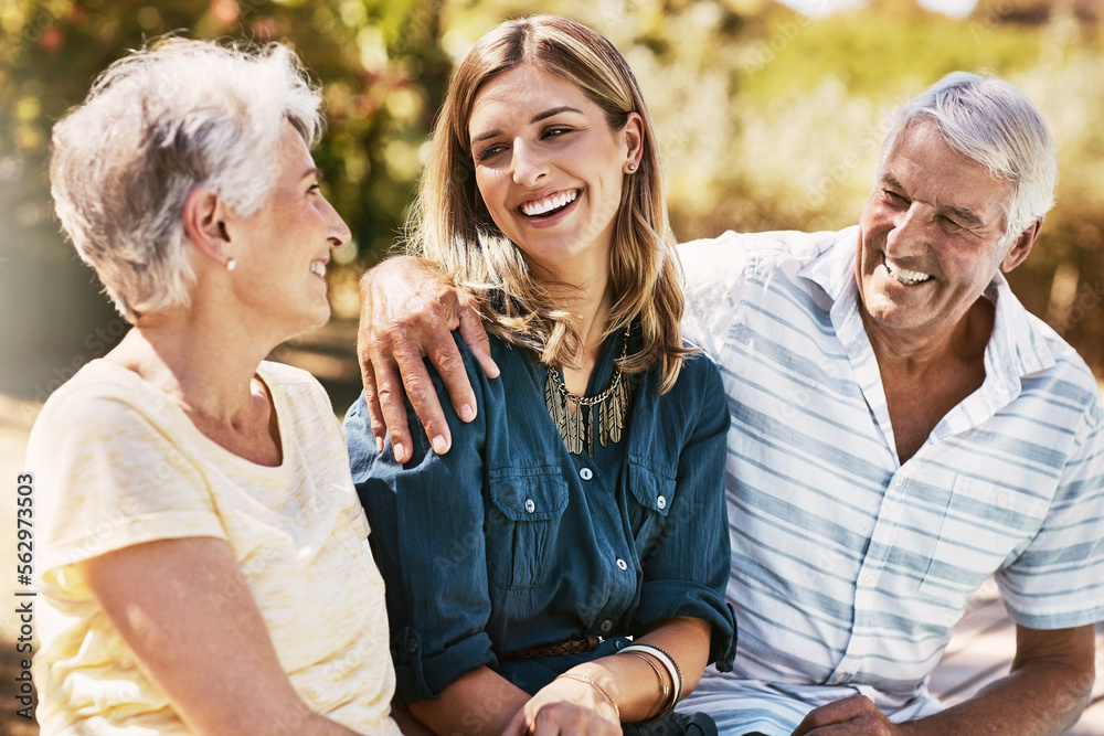 Senior parents in nature with their adult daughter sitting, talking and bonding together in a garden