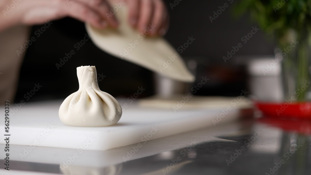 The chefs hands sculpt khinkali against the background of handmade cutting boards. Delicious homema