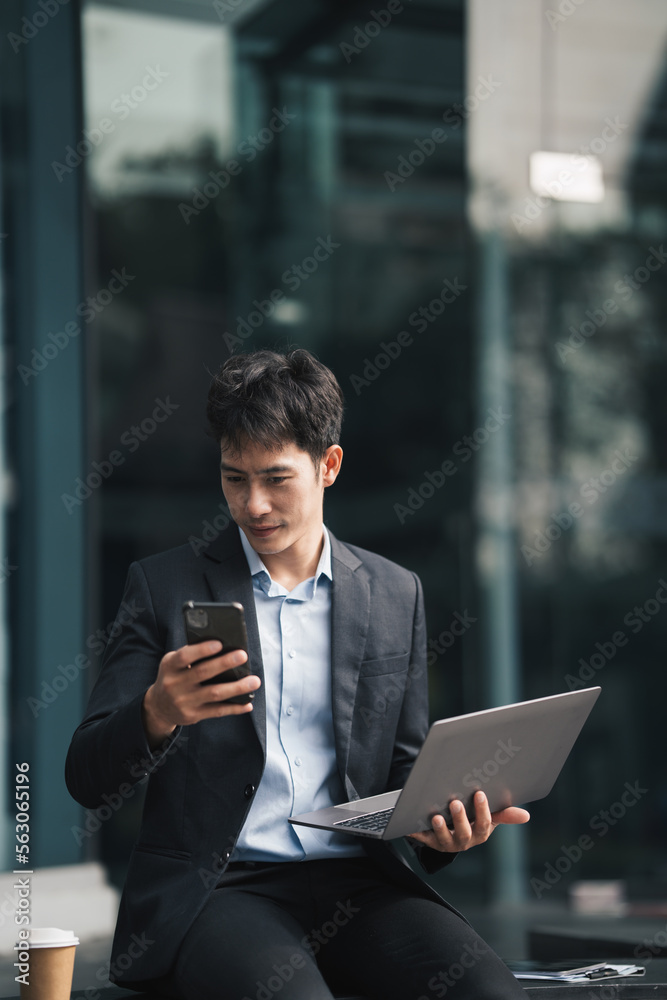 Handsome young manager working on laptop while sitting outdoors on the stairs, concept of work life 