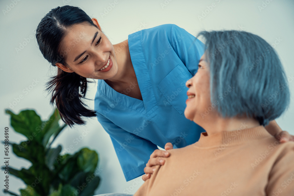 A caregiver rest her hands on the shoulders of a contented senior patient while she sitting on the s