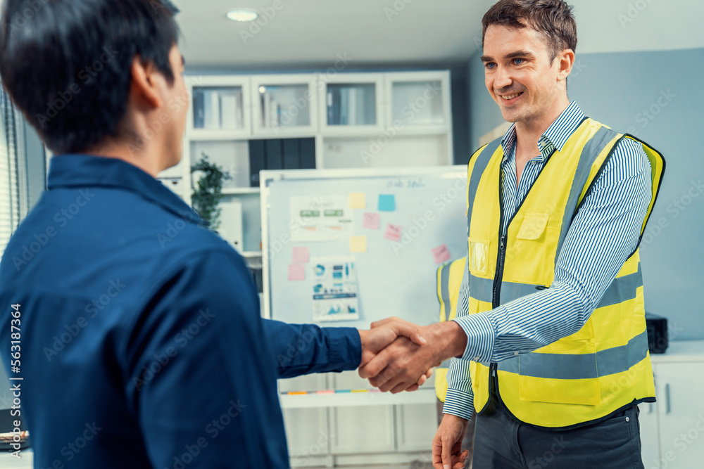 An engineer with a protective vest handshake with an investor in his office. Following a successful 