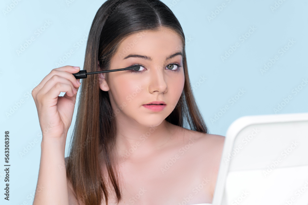 Closeup portrait of young charming applying makeup eyeshadow on her face with brush, mascara with fl