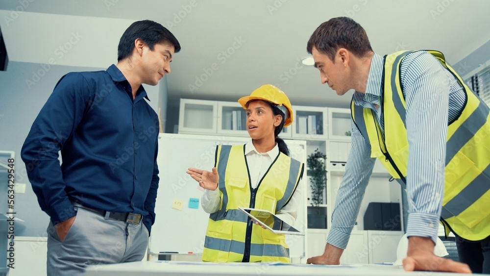 Engineers and competent employer discussing plans and blueprints together with tablet in the office.