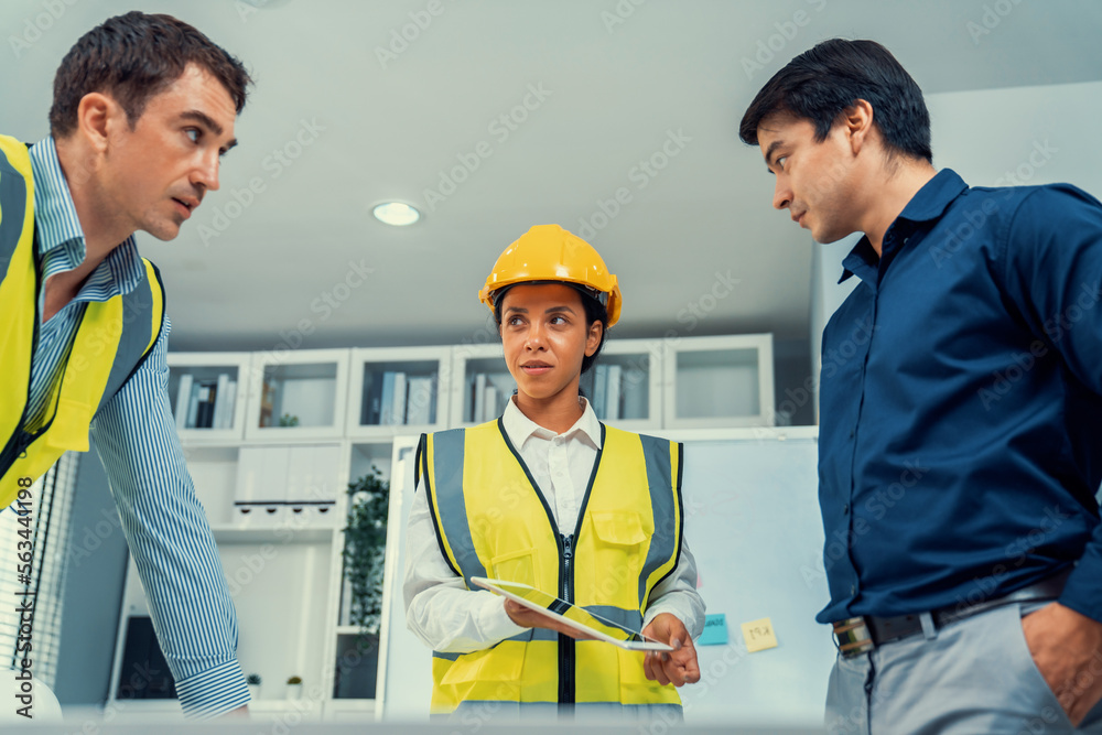 A team of competent engineers wearing safety equipment is working on blueprints with a tablet while 