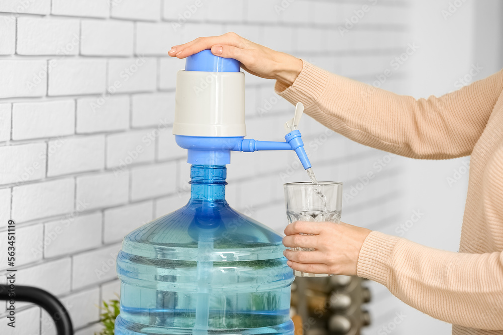 Woman pouring clean water from bottle into glass in kitchen, closeup