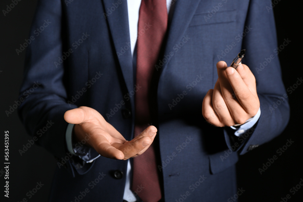 Young businessman with pen on black background, closeup