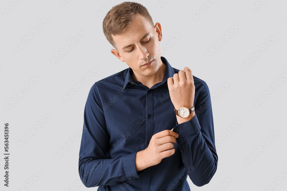 Young businessman adjusting shirt on light background