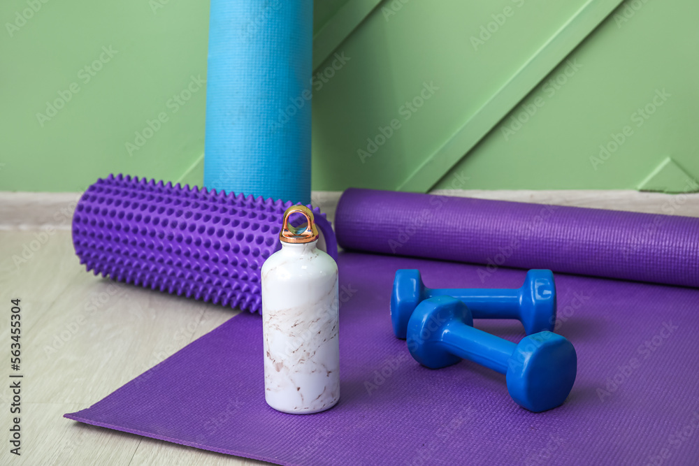 Sports water bottle with equipment on mat near green wall