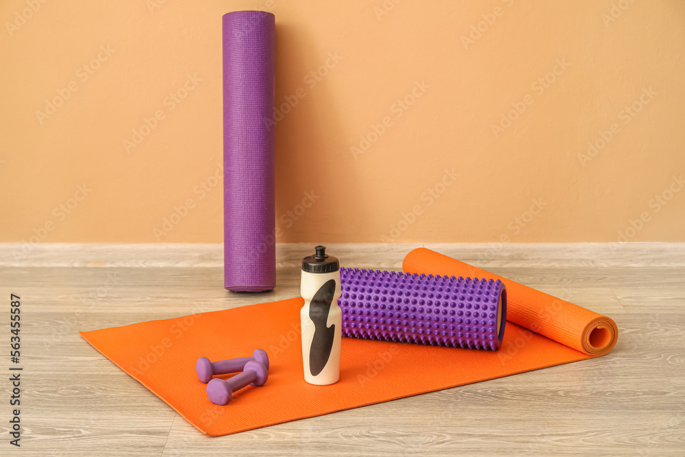 Sports water bottle with equipment on mat near beige wall