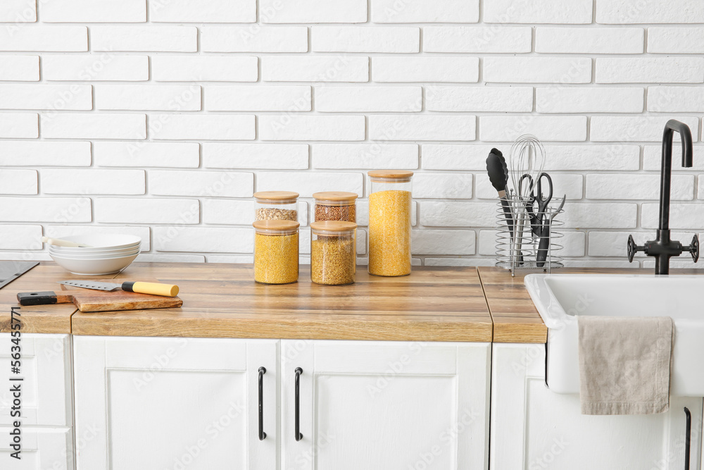 Jars with cereals on wooden table near light brick wall