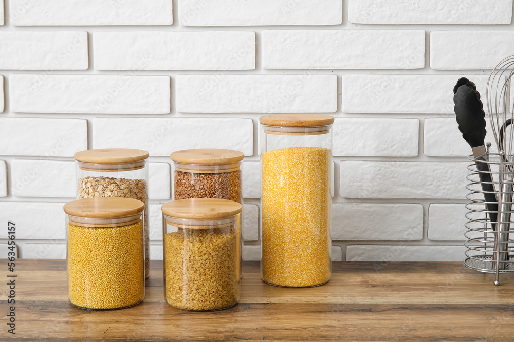 Jars with different cereals on wooden table near brick wall