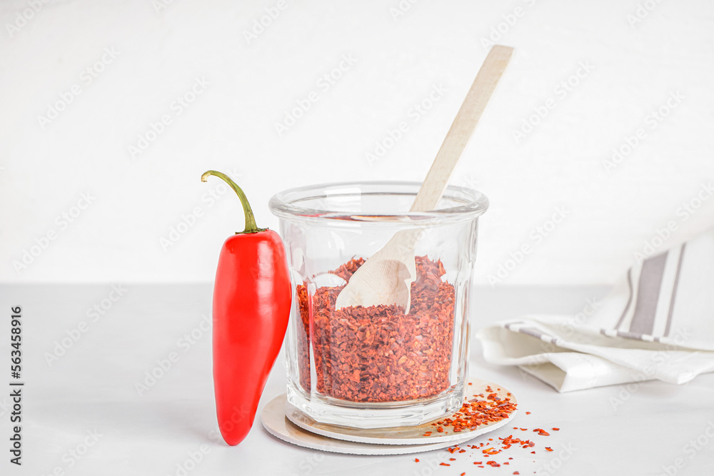 Glass with chipotle chili flakes on light background