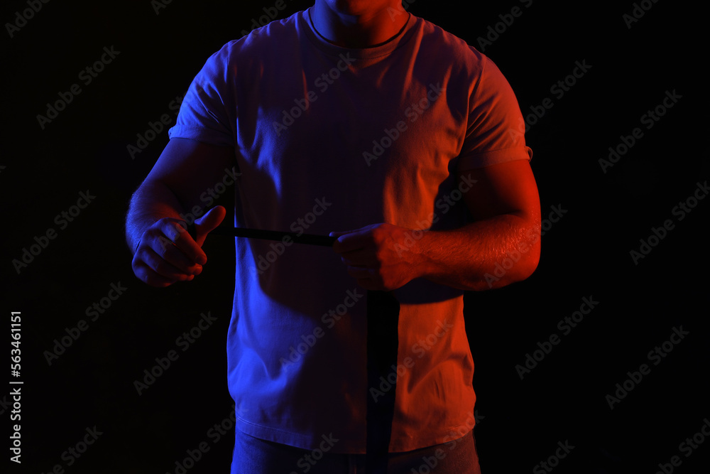 Silhouette of muscular young man with athletic tape on black background