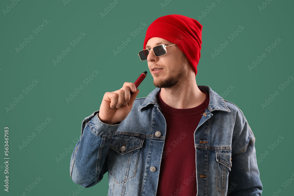 Stylish young man with disposable electronic cigarette on green background