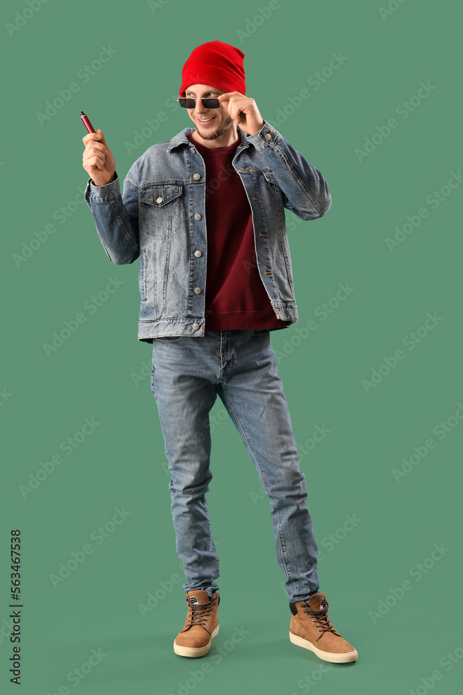 Stylish young man with disposable electronic cigarette on green background