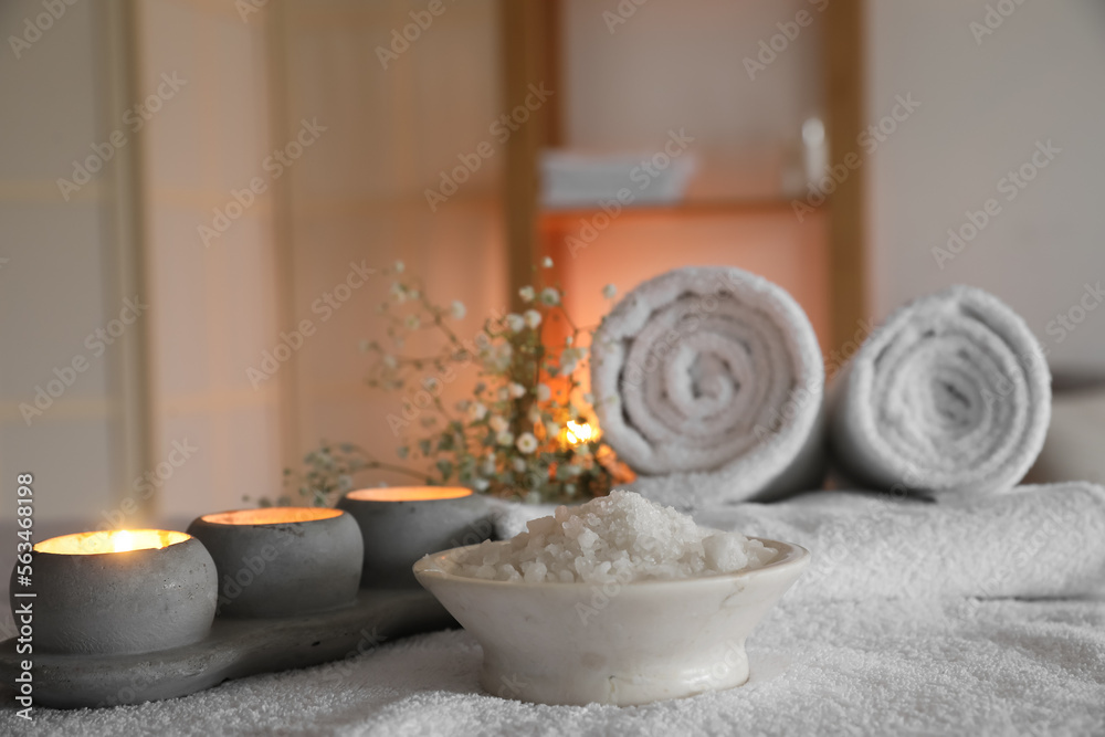 Bowl of sea salt and burning candles on couch in spa salon, closeup