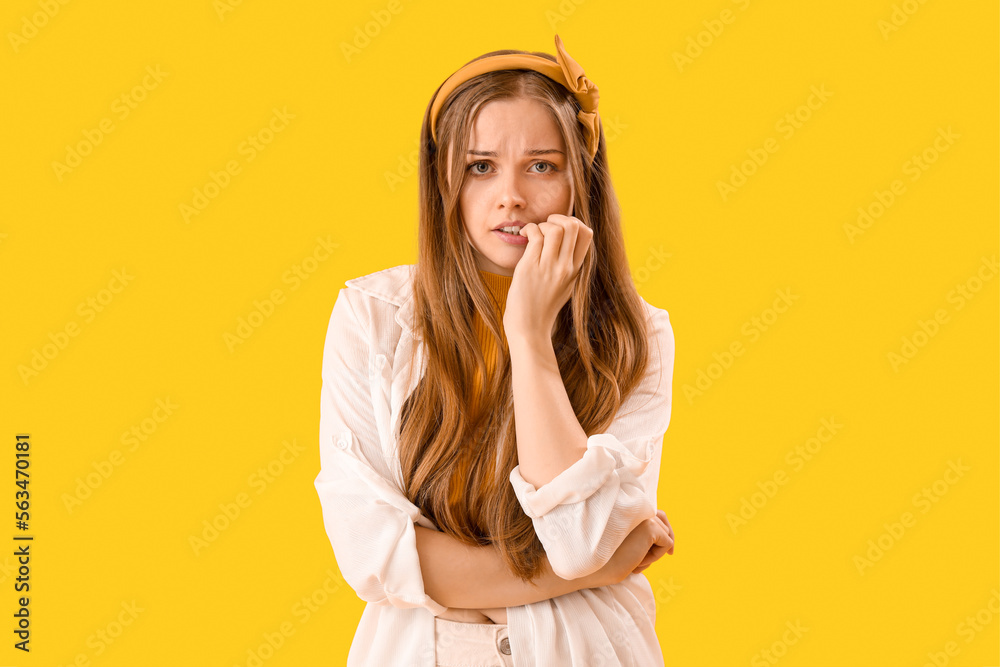 Young woman biting nails on yellow background