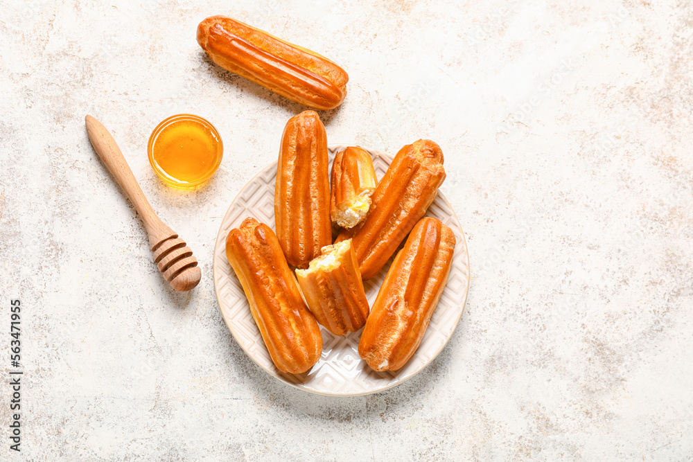 Plate with tasty eclairs and honey on light background