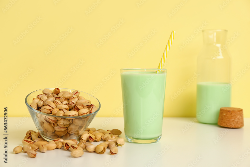 Glass of pistachio milk and bowl with nuts on yellow background