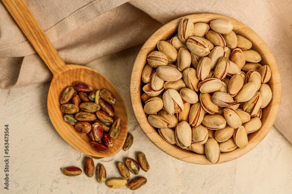 Bowl with pistachio nuts and spoon with kernels on light background