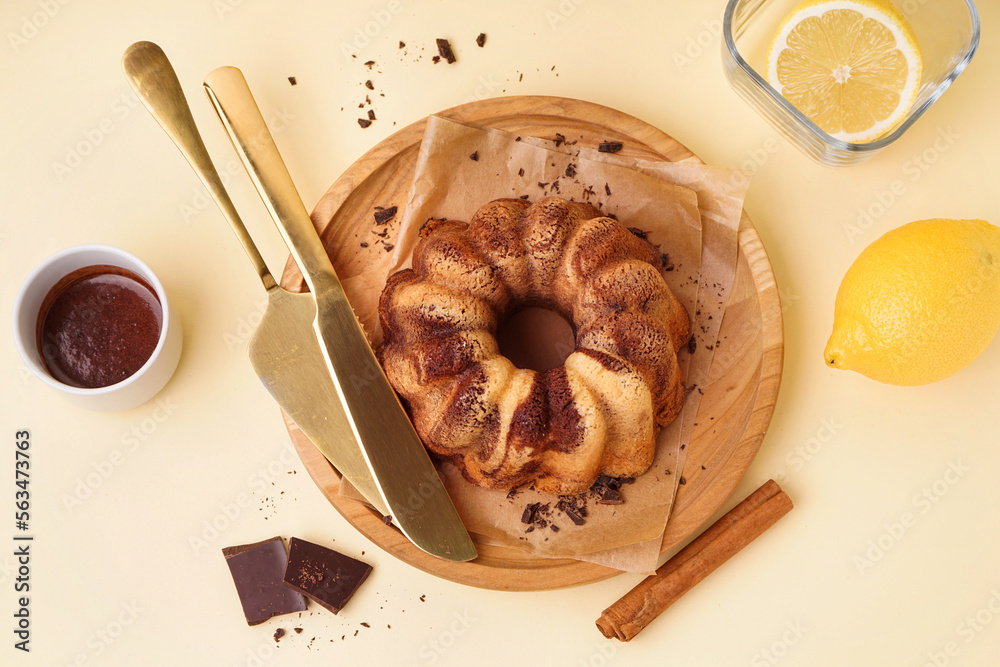 Wooden plate with delicious cake, cup of hot chocolate, lemon and cinnamon on yellow background