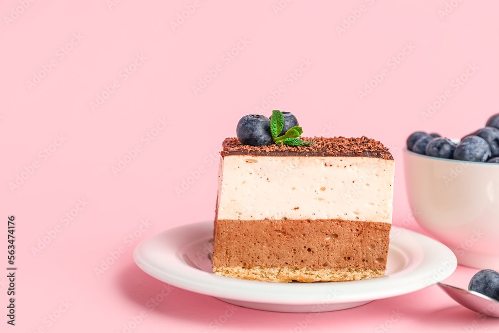 Plate with piece of birds milk cake, bowl of blueberries and spoon on pink background