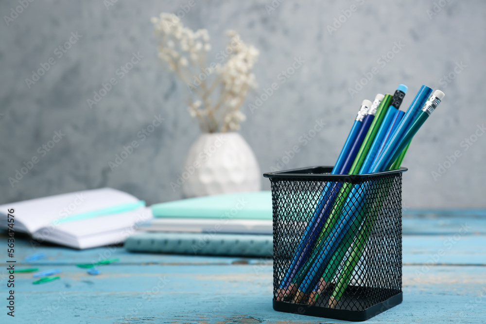 Holder with stationery, notebooks and vase with flowers on wooden background