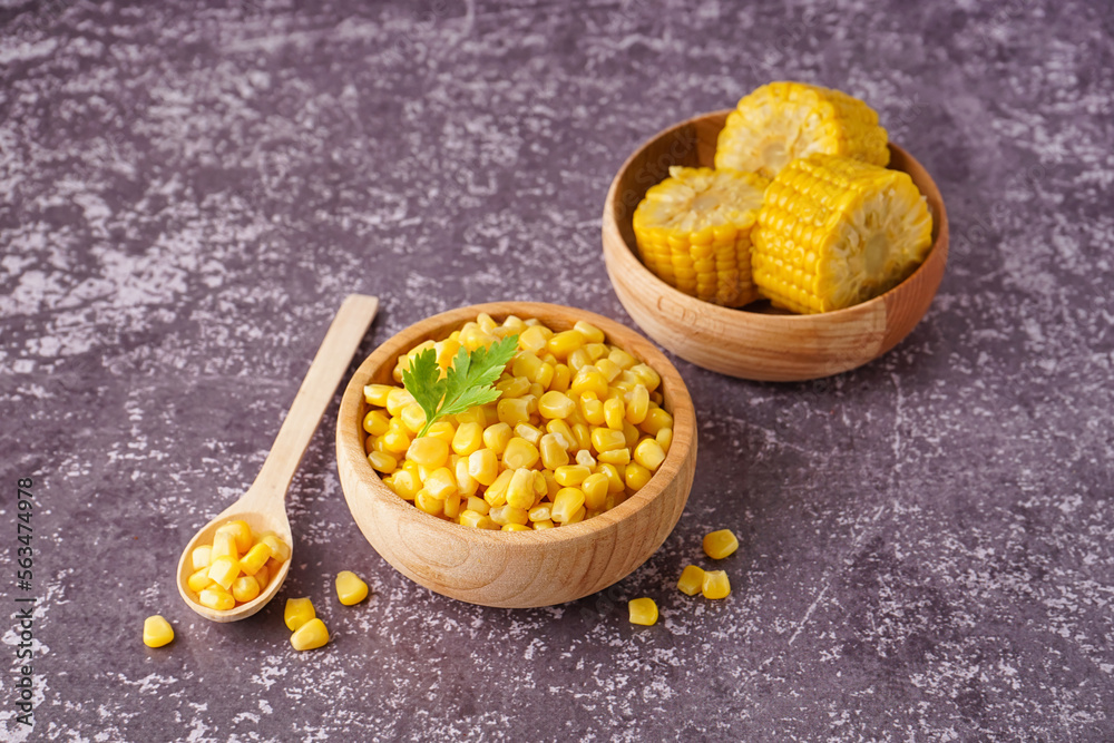 Bowls with canned corn kernels, cobs, parsley leaf and spoon on table