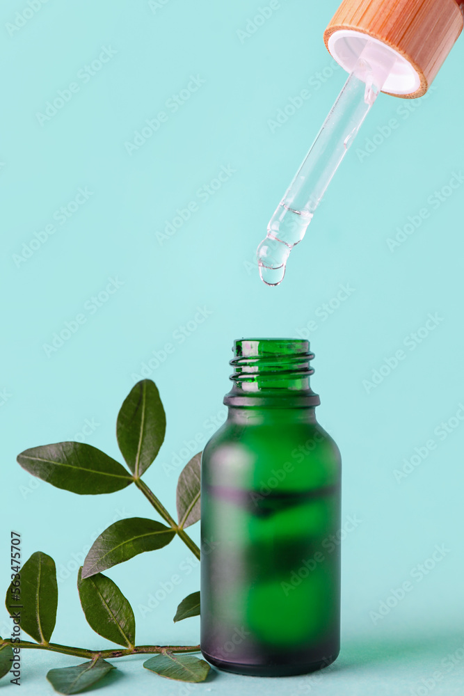 Bottle of serum with dropper and plant leaves on color background