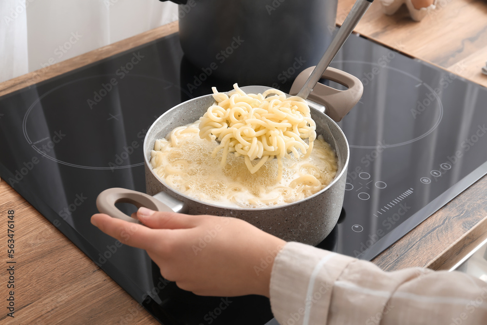 Woman cooking tasty pasta on stove in kitchen