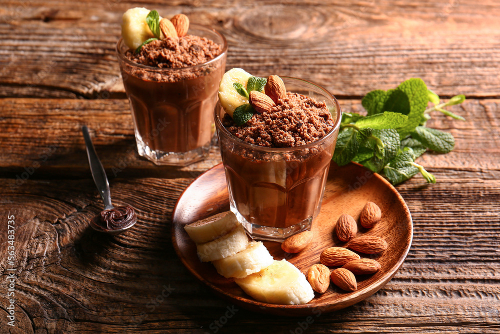 Glasses with delicious chocolate pudding, almond, banana and mint leaves on wooden background