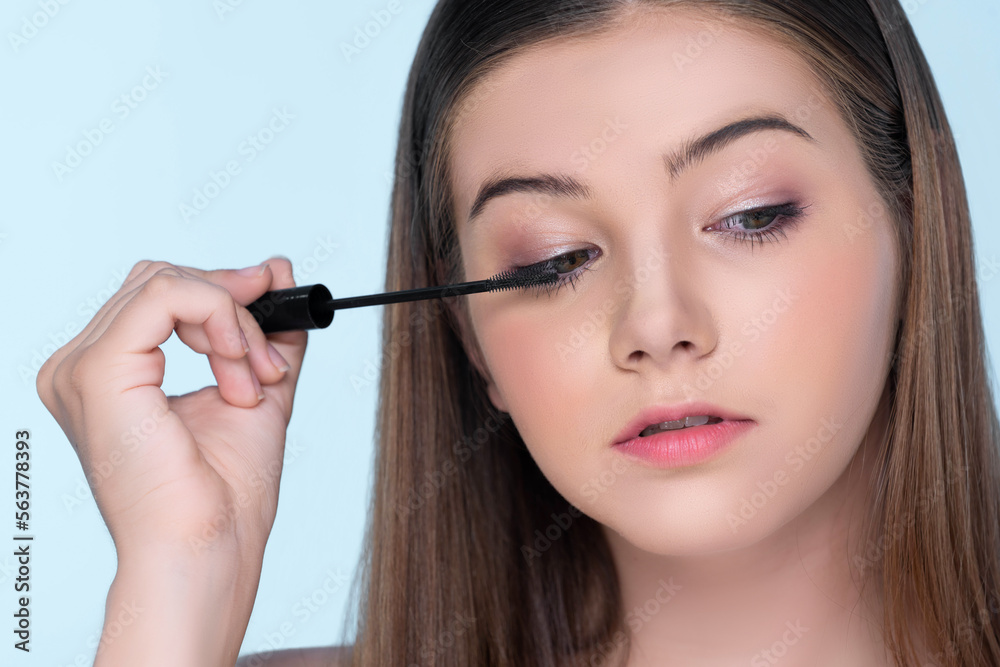 Closeup portrait of young charming applying makeup eyeshadow on her face with brush, mascara with fl