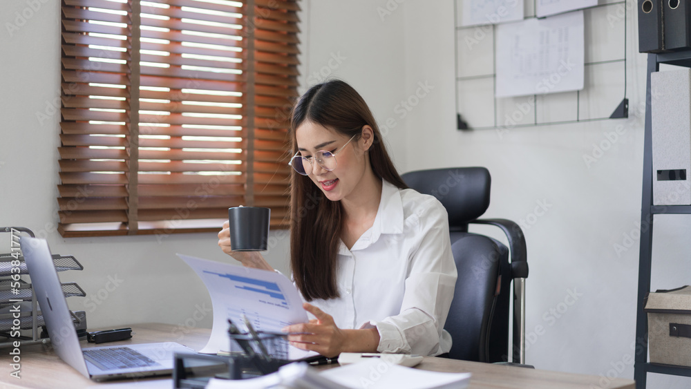 Business concept, Businesswoman is reading financial document and drinking coffee in modern office