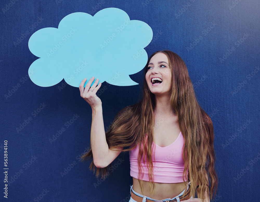 Happy woman holding a speech bubble with mockup space standing by a blue wall with a sign. Gen z, ha