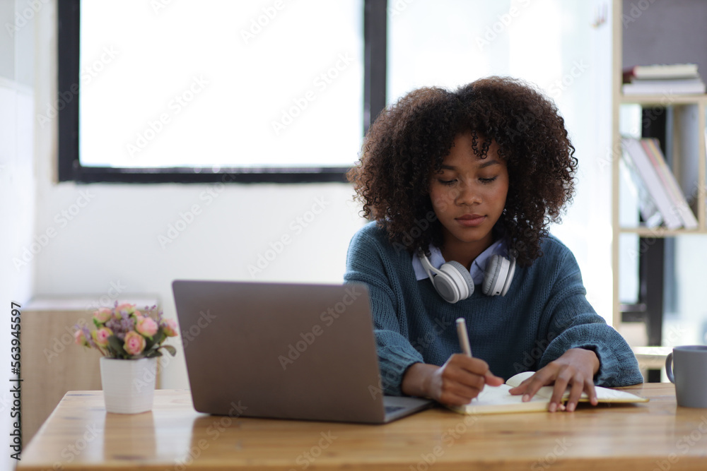 Portrait of young african woman working with laptop and reading books preparing for exams at her hom