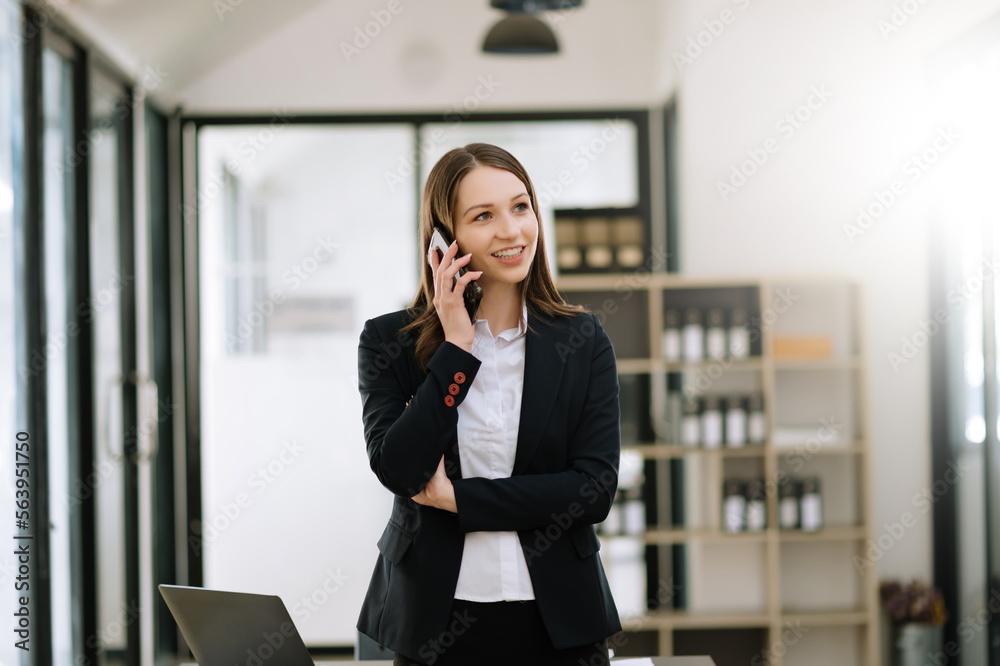 Business woman Talking on the phone and using a laptop with a smile while sitting at office.