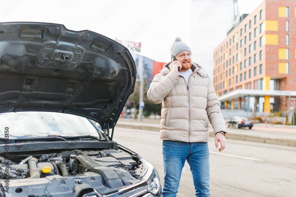 A lone man, looking unhappy and stressed, stands by his damaged vehicle on the side of the road,